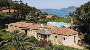 Uma vila em estilo mediterrâneo com piscina, rodeada por vegetação exuberante e vista para o mar.
