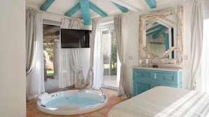 A bedroom with a large bed, a bathtub, a vanity with a mirror, and a television. - Villa Padulella 8 2 Emma Villas (Portoferraio)