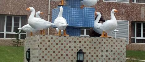 A sculpture of white ducks on a tiled structure with a building in the background.
