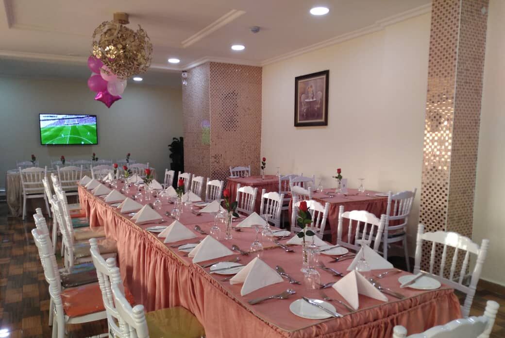 A banquet hall with long tables set for a formal event, white chairs, and a television displaying a sports game.