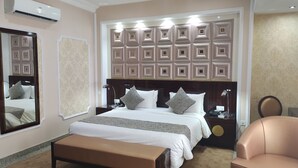 A hotel room with a large bed, a bedside table, a nightstand, a bench, and a chair. - Conference Hotel (Abeokuta)