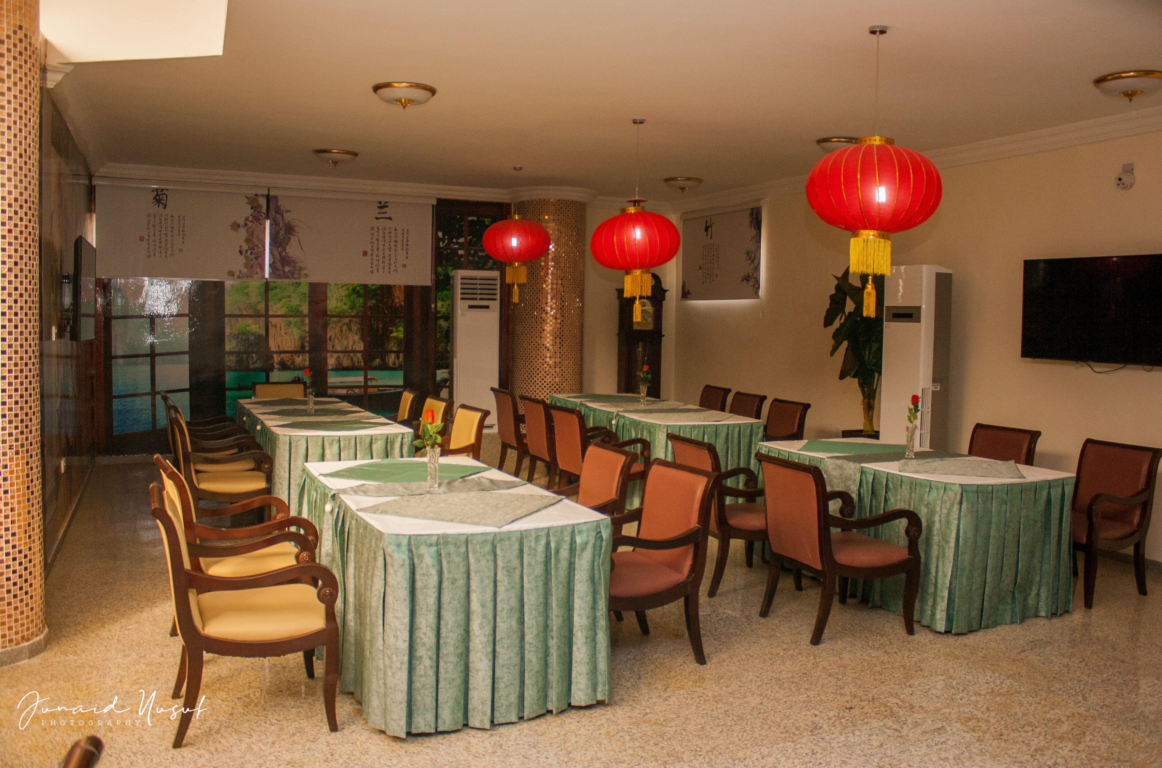 A dining area with tables covered in green tablecloths, wooden chairs, and red lanterns.