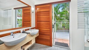 Un baño moderno con dos lavamanos, un espejo grande y una puerta corredera de vidrio que da a un balcón con vistas a palmeras.