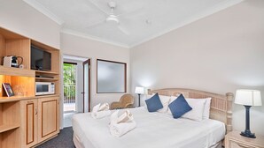 Habitación de hotel con una cama grande, un armario de madera, un televisor de pantalla plana, un microondas y una puerta que da a un balcón.