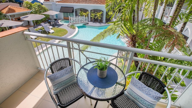 A balcony with a glass table, two chairs, and a potted plant. - 3 Bedroom Apartment 208 in Alassio Palm Cove (Cairns)