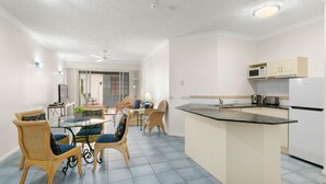 A modern kitchen with a central island, dining area with wicker chairs, and a ceiling fan. - 3 Bedroom Apartment 208 in Alassio Palm Cove (Cairns)