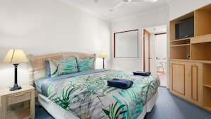 A bedroom with a bed, nightstands, a ceiling fan, a TV, and a wooden wardrobe. - 3 Bedroom Apartment 208 in Alassio Palm Cove (Cairns)