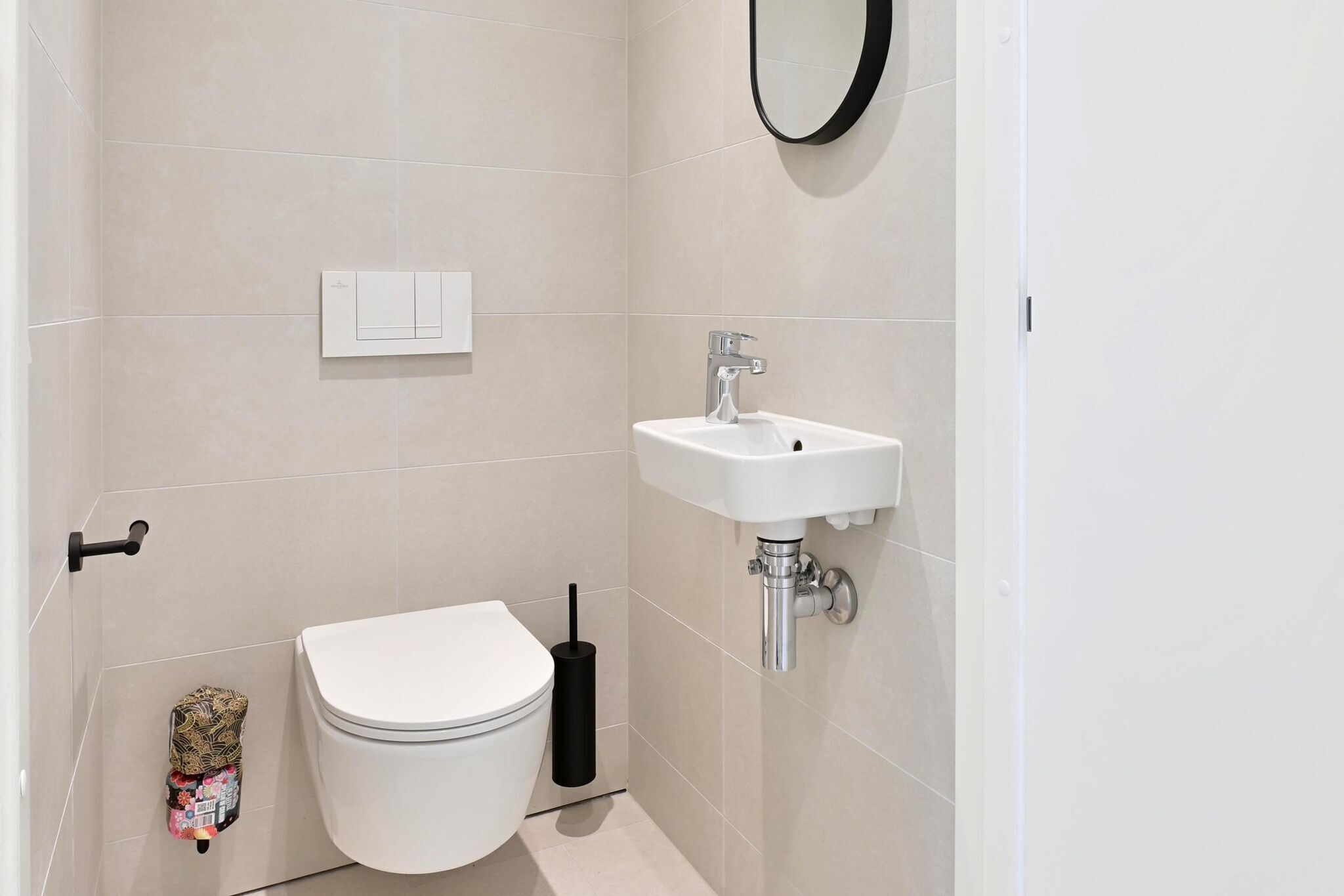 Une petite salle de bain propre, équipée de toilettes, d’un lavabo et d’une brosse à récurer les toilettes.
