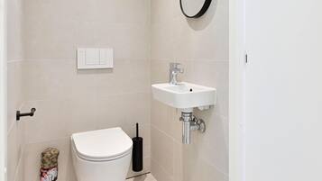 Une petite salle de bain propre, équipée de toilettes, d’un lavabo et d’une brosse à récurer les toilettes.