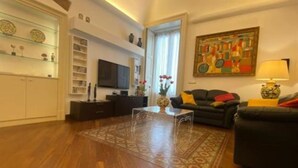 A living room with a wooden floor, a glass coffee table, a black sofa, a TV, and a painting on the wall. - Luxury Suite Center (Catania)