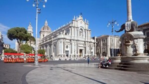 A large open square with a prominent white cathedral, a statue, and a tram. - Luxury Suite Center (Catania)