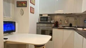 A compact kitchen with white cabinets, a microwave, and a small dining area with a stool. - Luxury Suite Center (Catania)