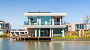 A modern two-story house with large glass windows, a wooden deck, and a view of a calm body of water. - Waterfront holiday home in Arnemuiden (Arnemuiden)