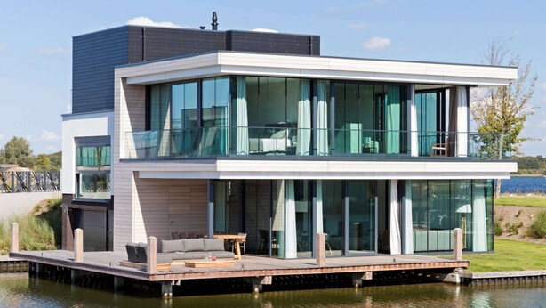 A modern two-story house with large glass windows, a wooden deck, and a view of the water. - Waterfront holiday home in Arnemuiden (Arnemuiden)