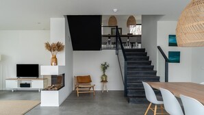 A modern living room with a flat-screen TV, a wooden bench, a small table with a vase, and a staircase leading to an upper level. - Waterfront holiday home in Arnemuiden (Arnemuiden)