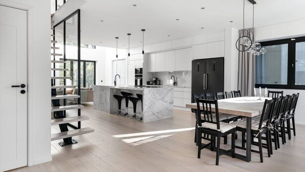 Una cocina moderna con una isla de mármol, taburetes negros y un comedor con mesa y sillas de madera.