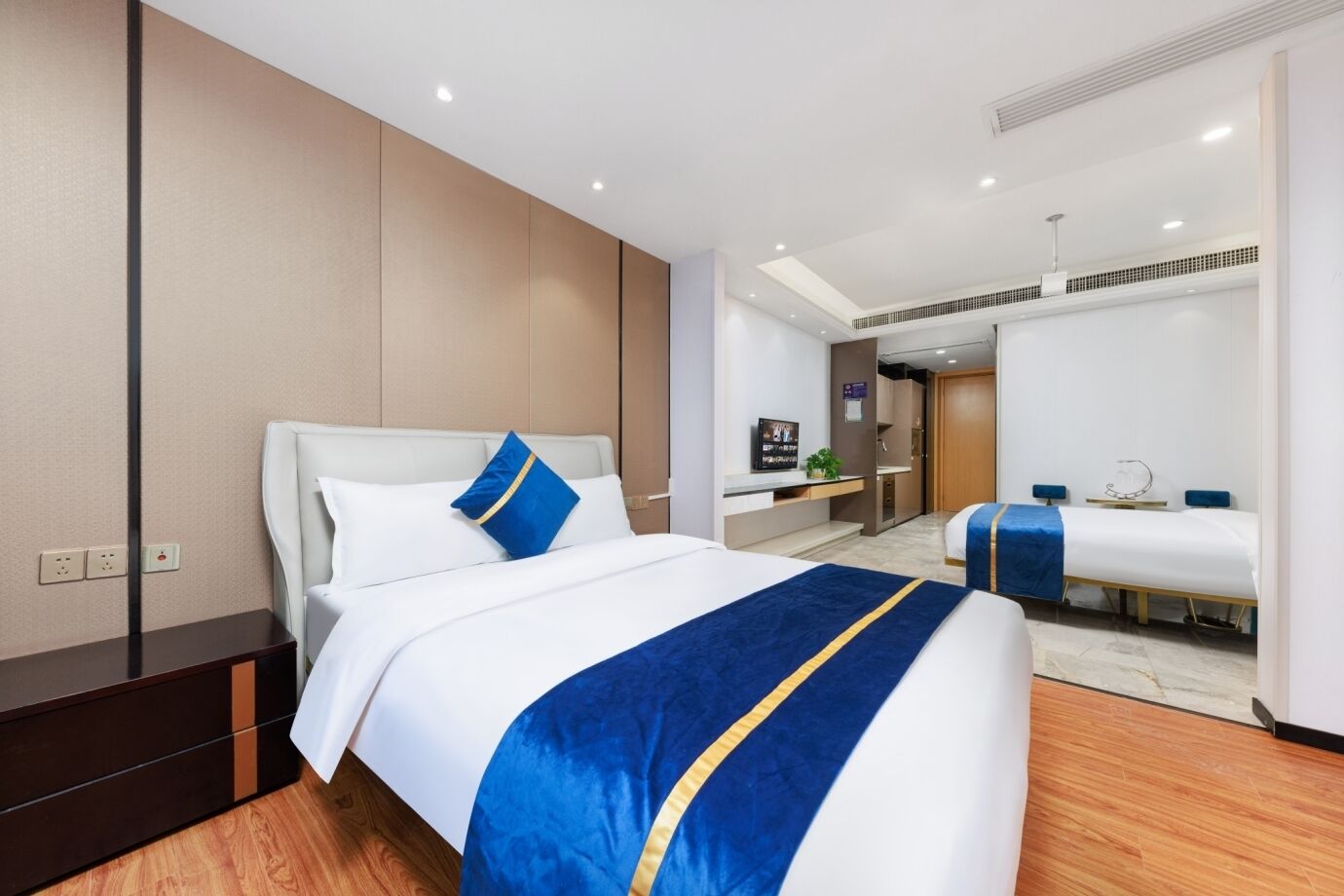 A hotel room with a large bed, a smaller bed, a desk, and a bathroom visible through an open door.