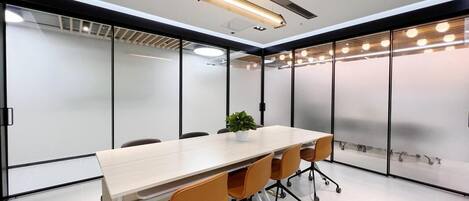 A modern conference room with a long table, orange chairs, and a potted plant.