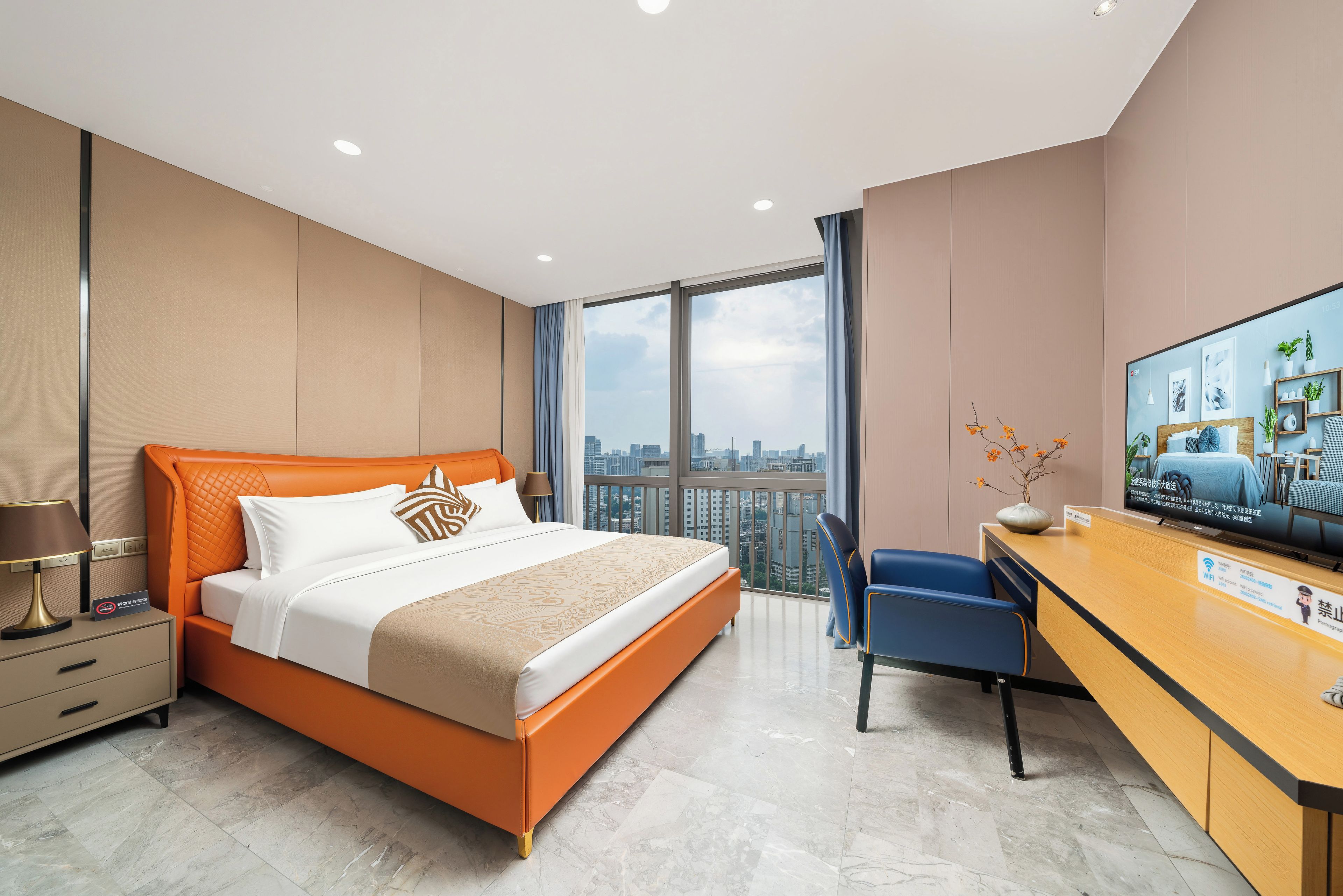 A hotel room with a bed, a desk, a chair, a television, and a view of the cityscape.