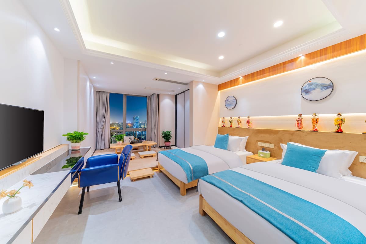 Quarto de hotel com duas camas, uma escrivaninha, cadeiras, televisão e vista para a cidade.