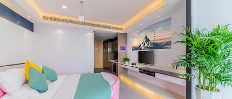 Une chambre d’hôtel moderne avec un lit aux lignes courbes, une télévision, une plante et une fresque murale.