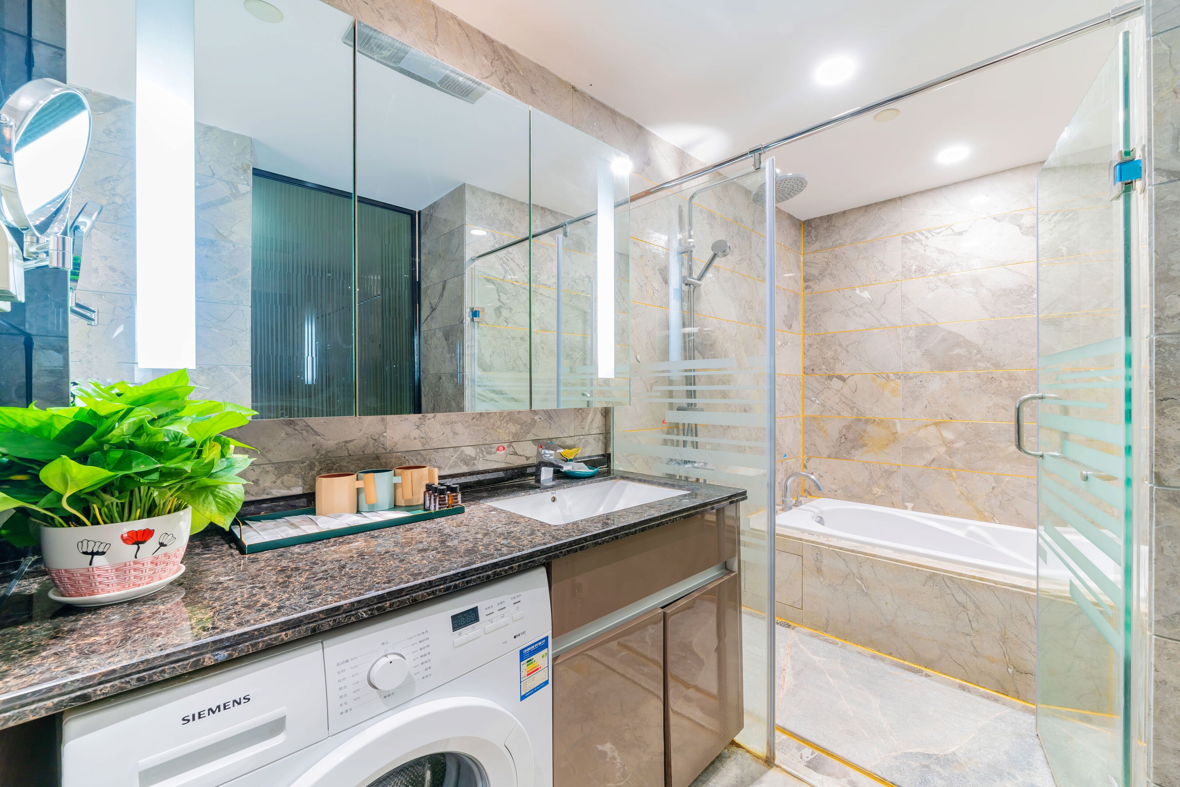 A modern bathroom with a glass shower enclosure, a built-in sink, and a white washing machine.