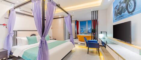 Una habitación de hotel moderna con cama con dosel, televisor de pantalla plana, zona de estar con mesa y sillas, y un ventanal con vistas a la ciudad.
