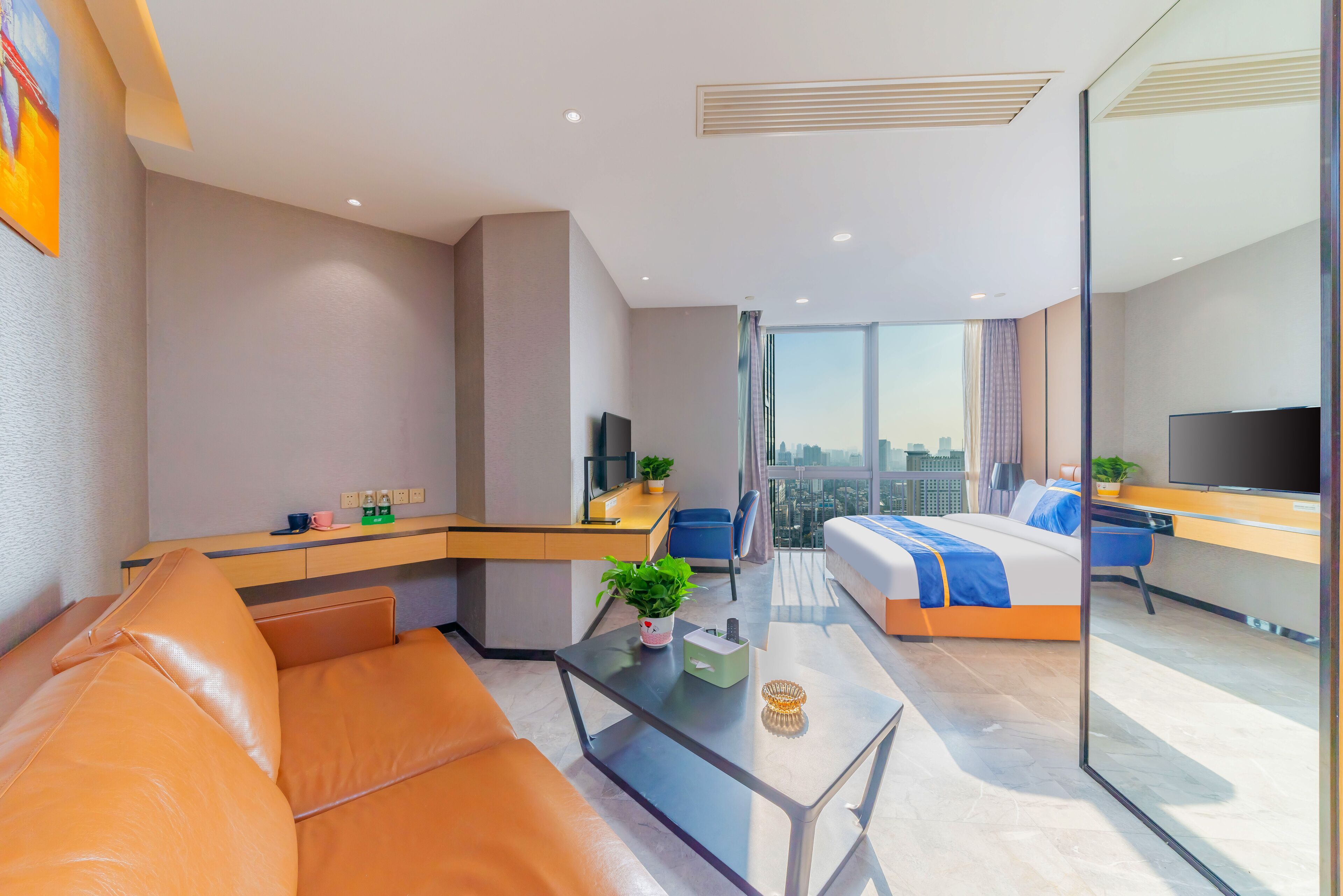A modern hotel room with a glass partition, a sofa, a bed, a desk, and a TV.