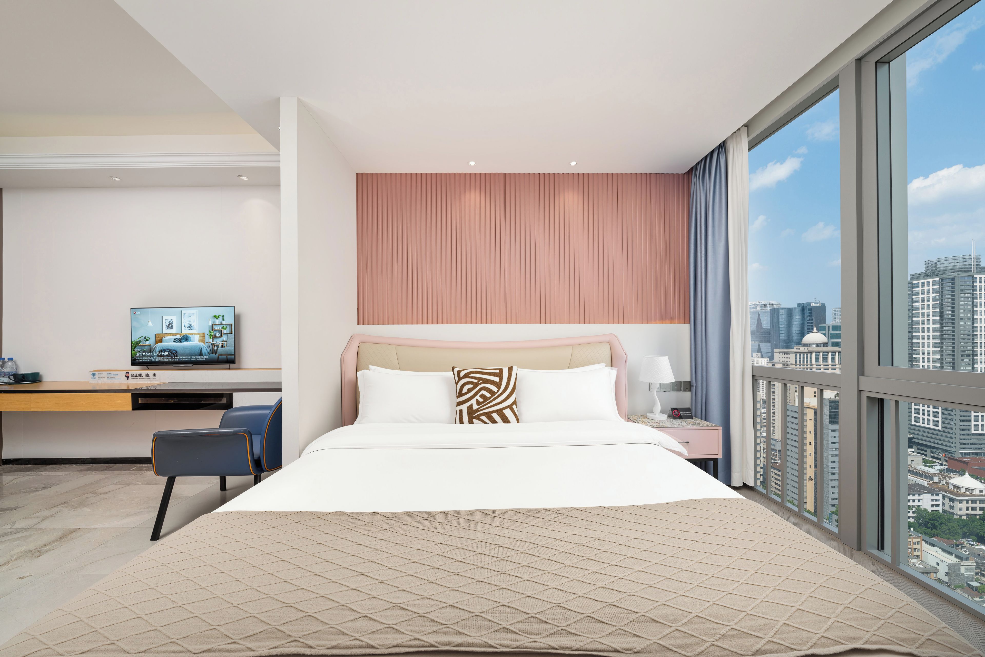 A hotel room with a large bed, a desk with a television, and a city view.