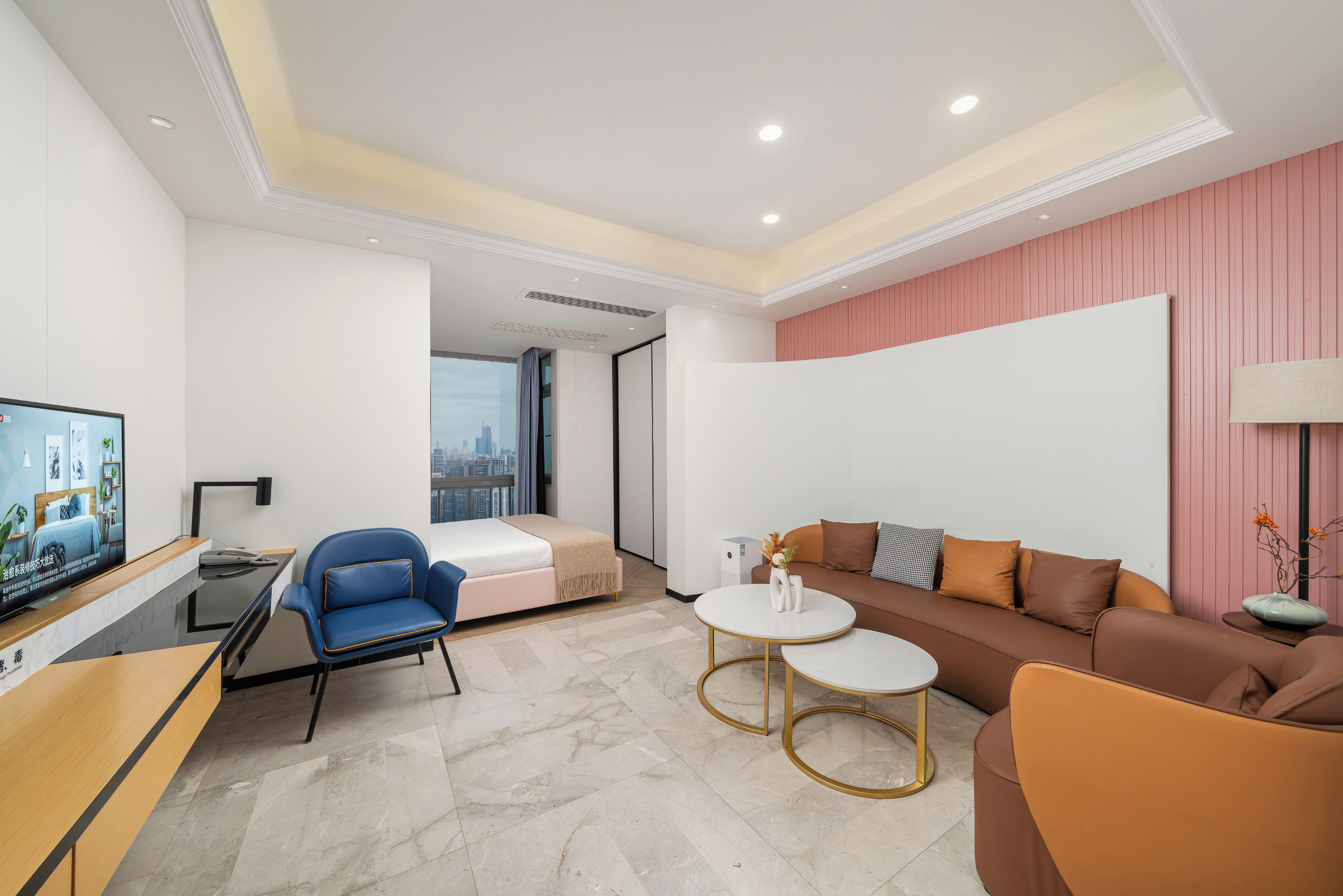 A modern hotel room with a bed, a sofa, a desk, and a TV.