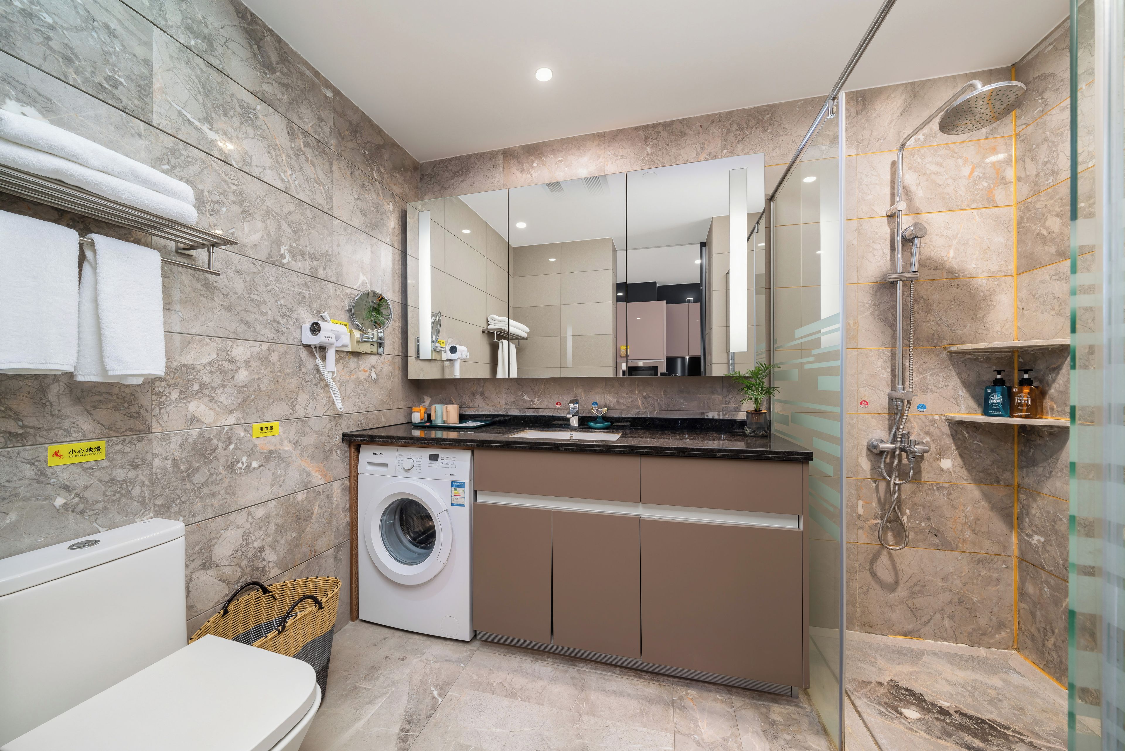 A modern bathroom with a built-in washing machine, a shower, and a mirror above the sink.