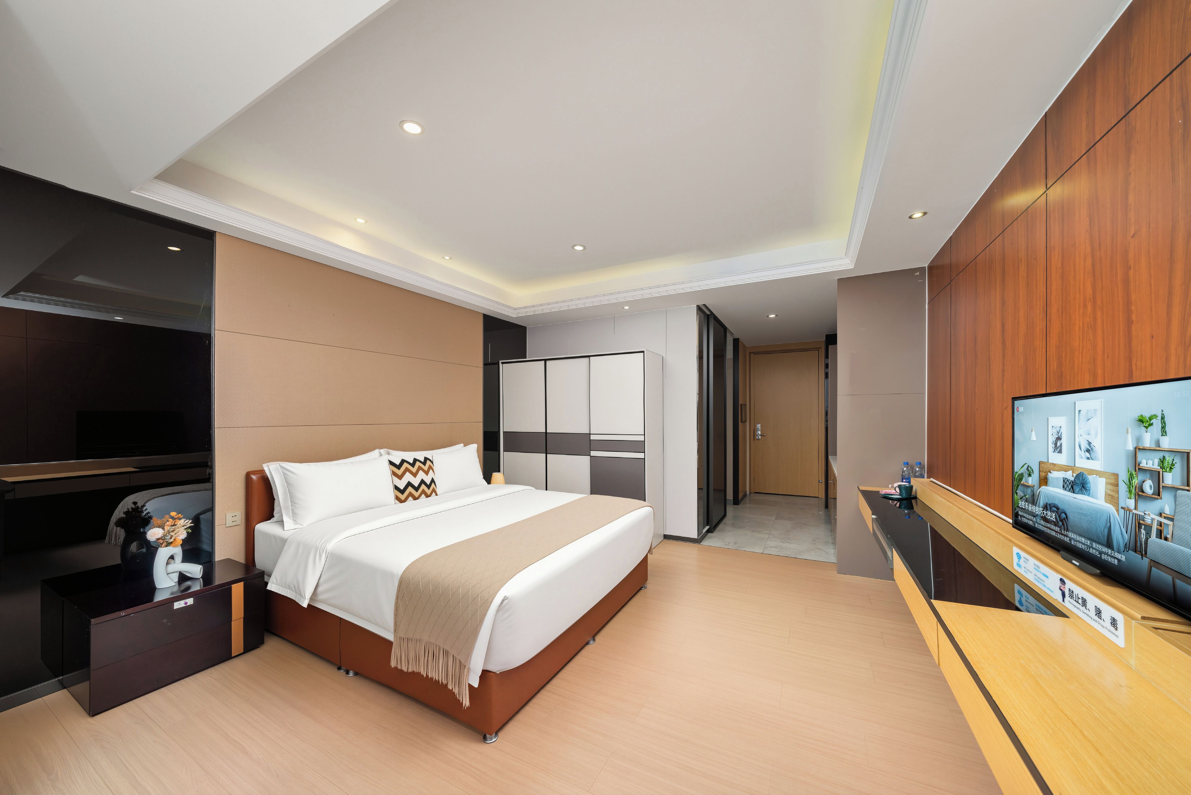 A modern hotel room with a large bed, a flat-screen TV, a desk, and a wardrobe.