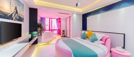 Un dormitorio moderno con una cama curvada, un televisor de pantalla plana y un ventanal con cortinas.