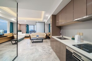 A modern hotel room with a sofa, a coffee table, a TV, a kitchen area with a sink and stove, and a city view. - Cloudy International Apartment (Guangzhou)