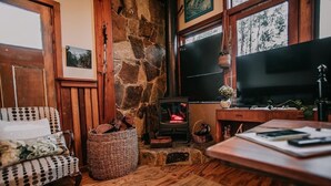 A cozy living room with a stone fireplace, a television, a wicker basket, and a patterned armchair. - CIRQUE 5 -  Two bedroom alpine lodge (Merrijig)