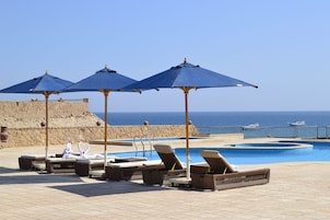 Un área junto a la piscina con sillones de descanso y sombrillas, un muro de piedra y vistas al mar.