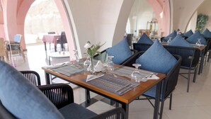 Un espace repas avec des tables préparées pour deux personnes, doté de chaises bleues rembourrées et d’un vase central orné de fleurs.