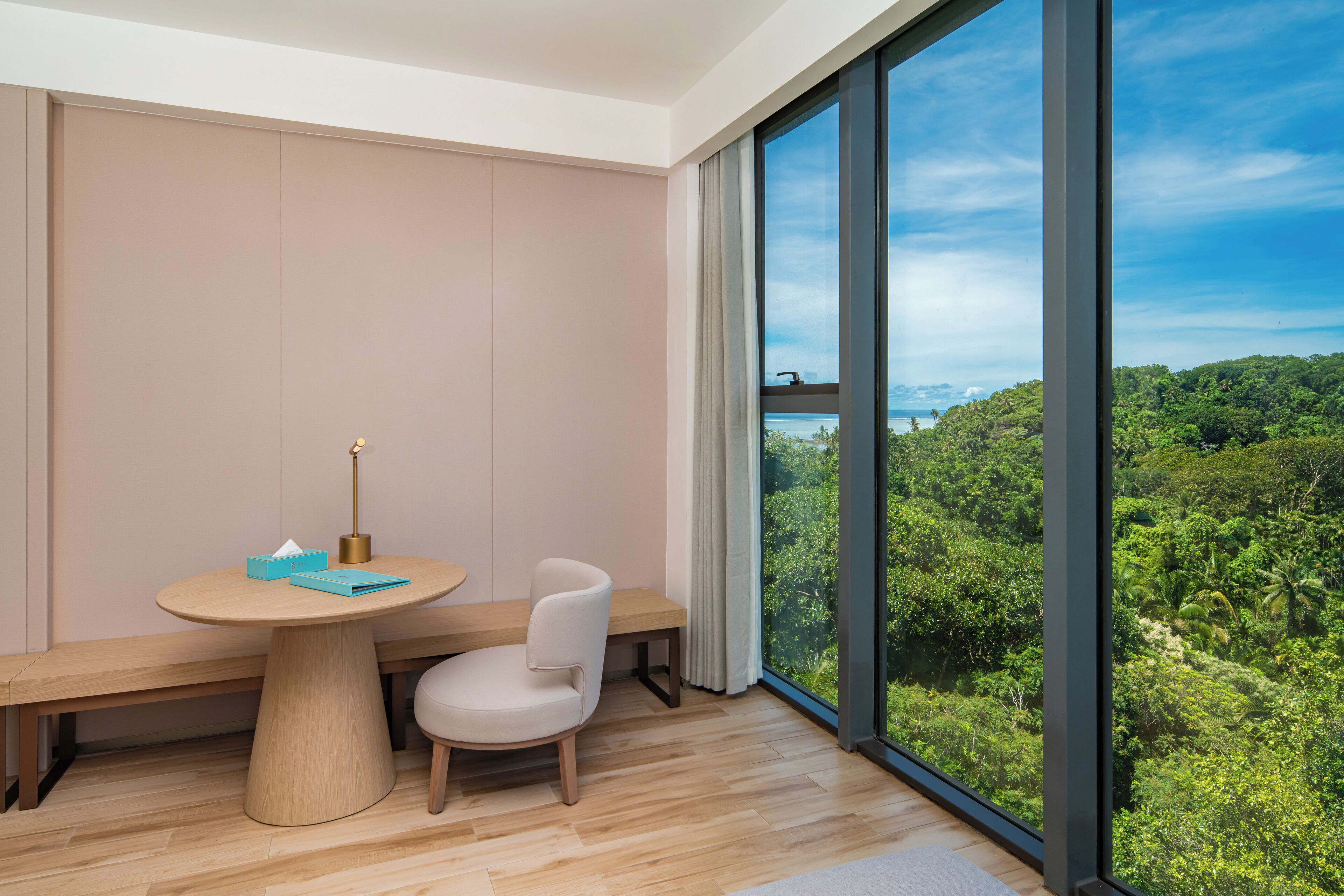 A modern room with a large window, a round table, a chair, and a view of a lush green landscape.