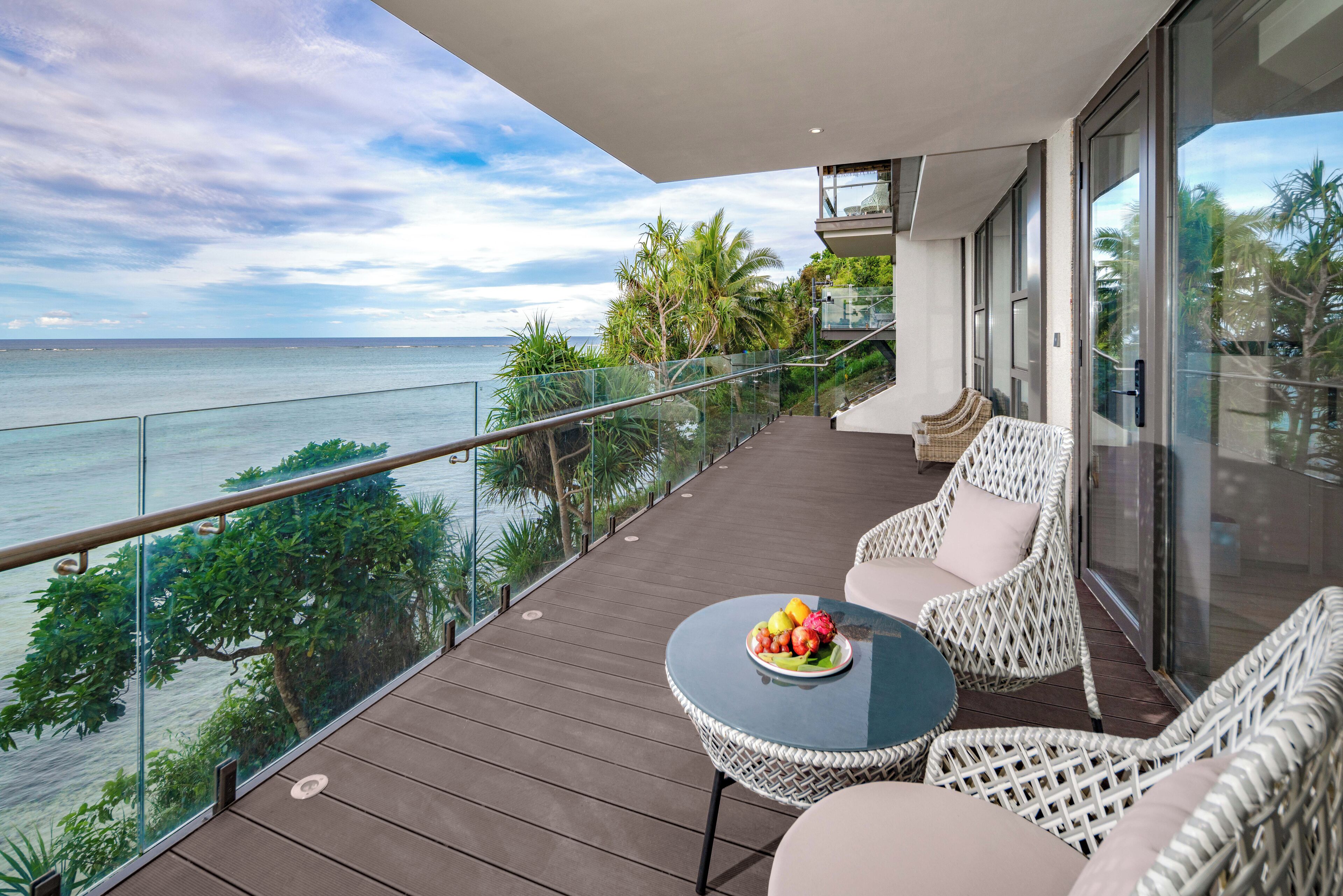 A balcony with wicker furniture, a table with fruit, and a view of the sea.
