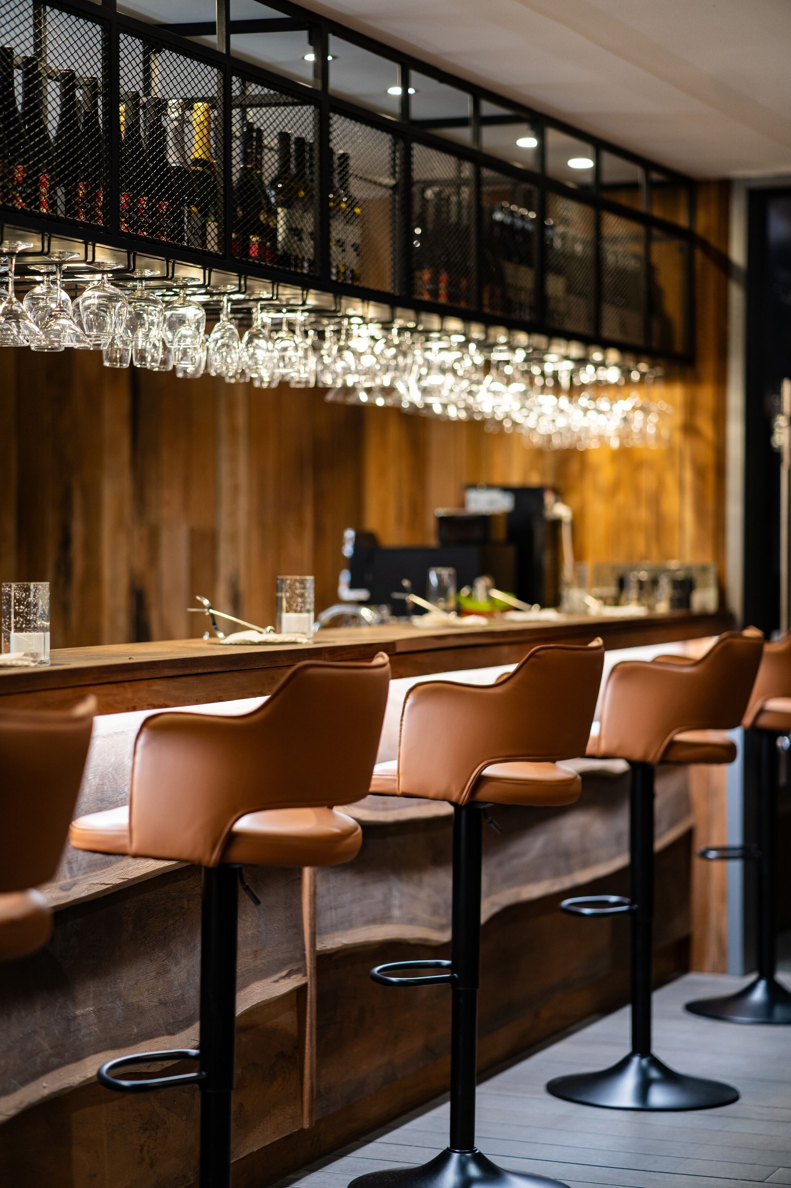 Zona de bar con mostradores de madera, taburetes de cuero y una lámpara colgante.