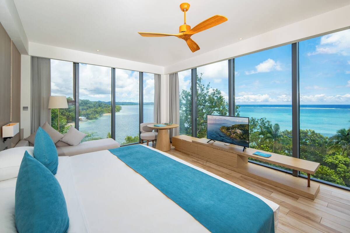 Ein modernes Hotelzimmer mit einem großen Bett, einem Fernseher, einer Sitzecke und Meerblick.
