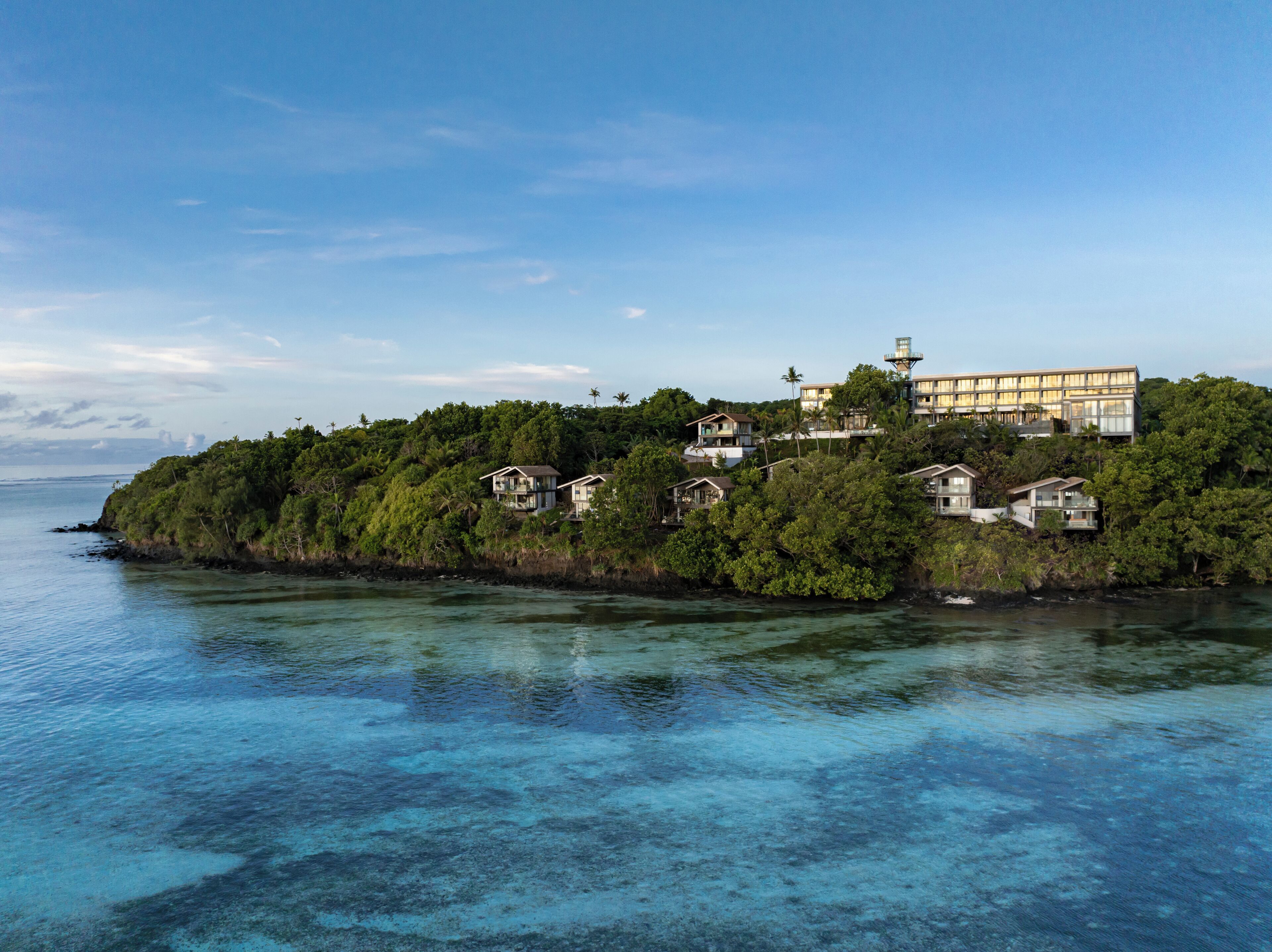 Una propiedad costera con varias casas en una pequeña isla, rodeada de aguas azules cristalinas y abundante vegetación.