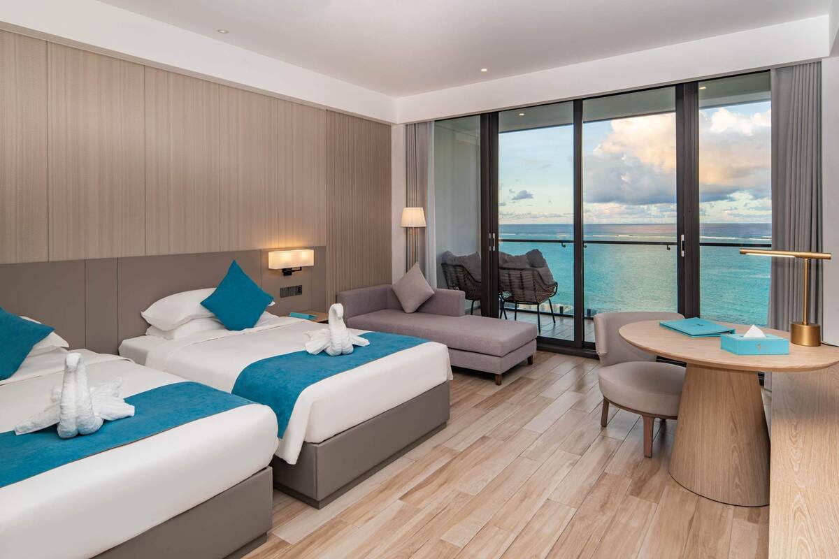 Ein modernes Hotelzimmer mit zwei Betten, einer Couch, einem Esstisch und Blick auf den Ozean.