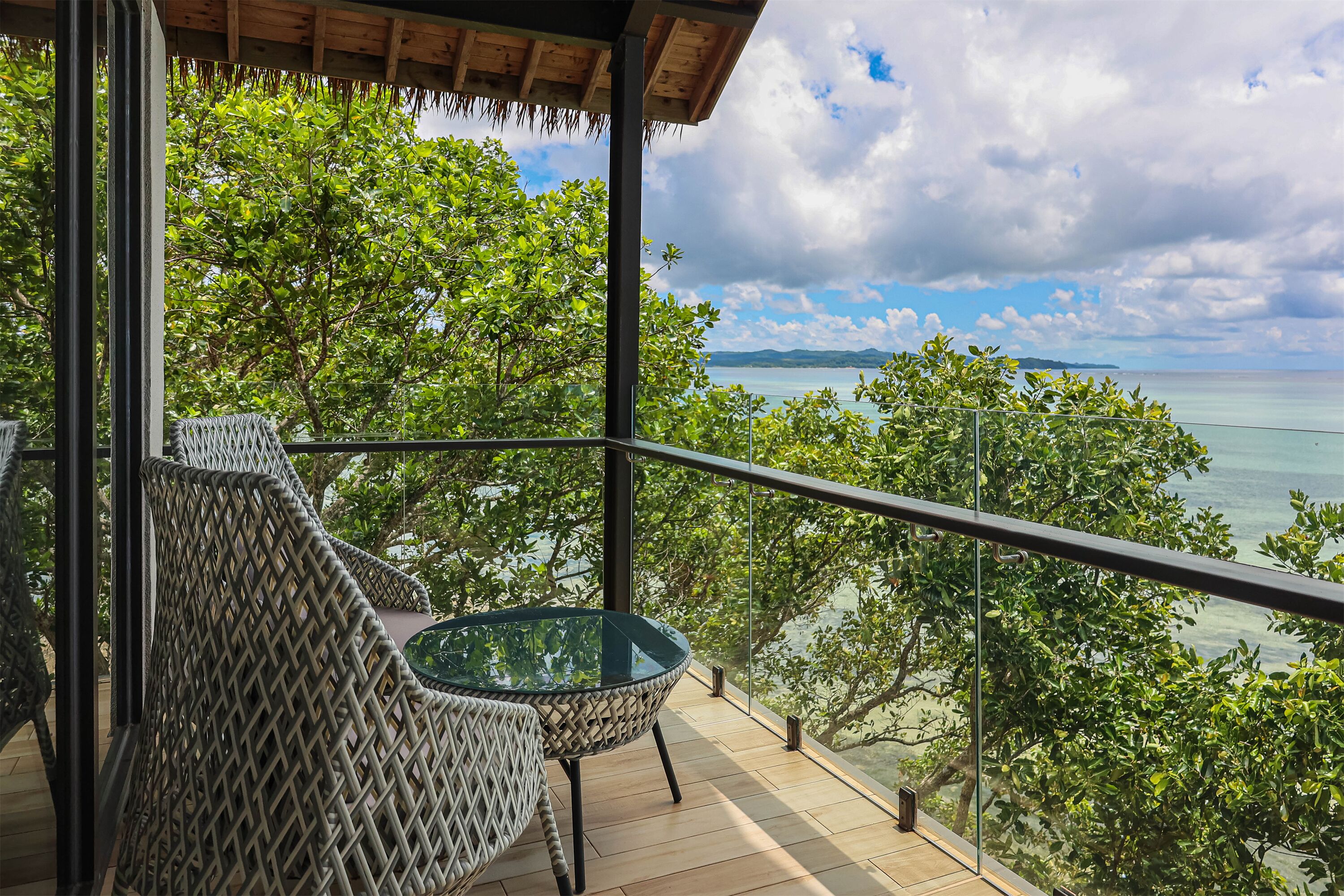 A balcony with wicker furniture overlooking a scenic view of the sea and lush greenery.