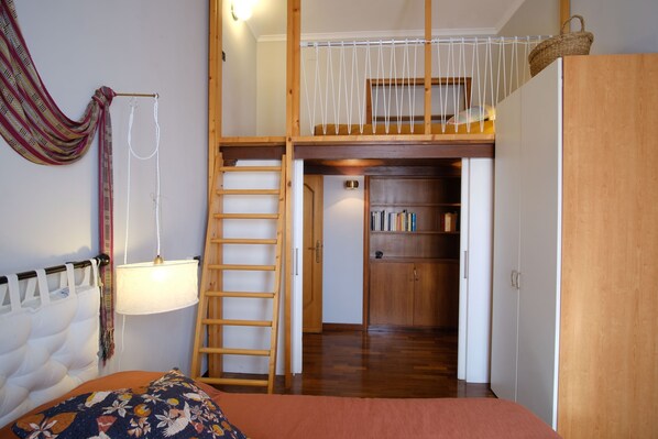 A bedroom with a loft bed, a ladder, a bookshelf, and a wardrobe.