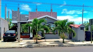 Un quartier résidentiel avec une maison à deux étages, une voiture garée et plusieurs palmiers.