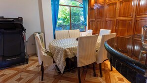 Un coin repas avec une table dressée pour quatre personnes, un tapis de course et une vue sur la verdure par une fenêtre.