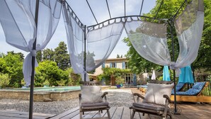 A wooden deck with two lounge chairs and a pergola with sheer fabric.
