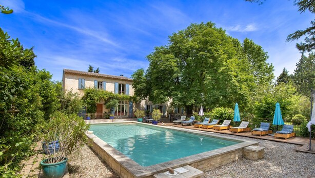 A rectangular swimming pool surrounded by a stone deck, with lounge chairs and umbrellas.