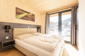 Una habitación de hotel moderna con una cama grande, paredes de madera, vistas a un paisaje nevado y un cuadro en la pared.